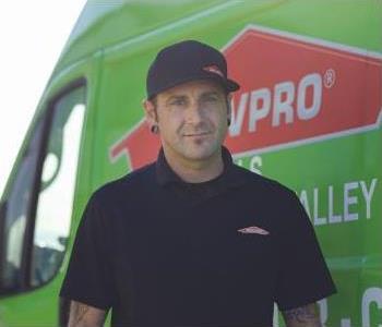Man wearing black shirt and hat standing in front of a green van.